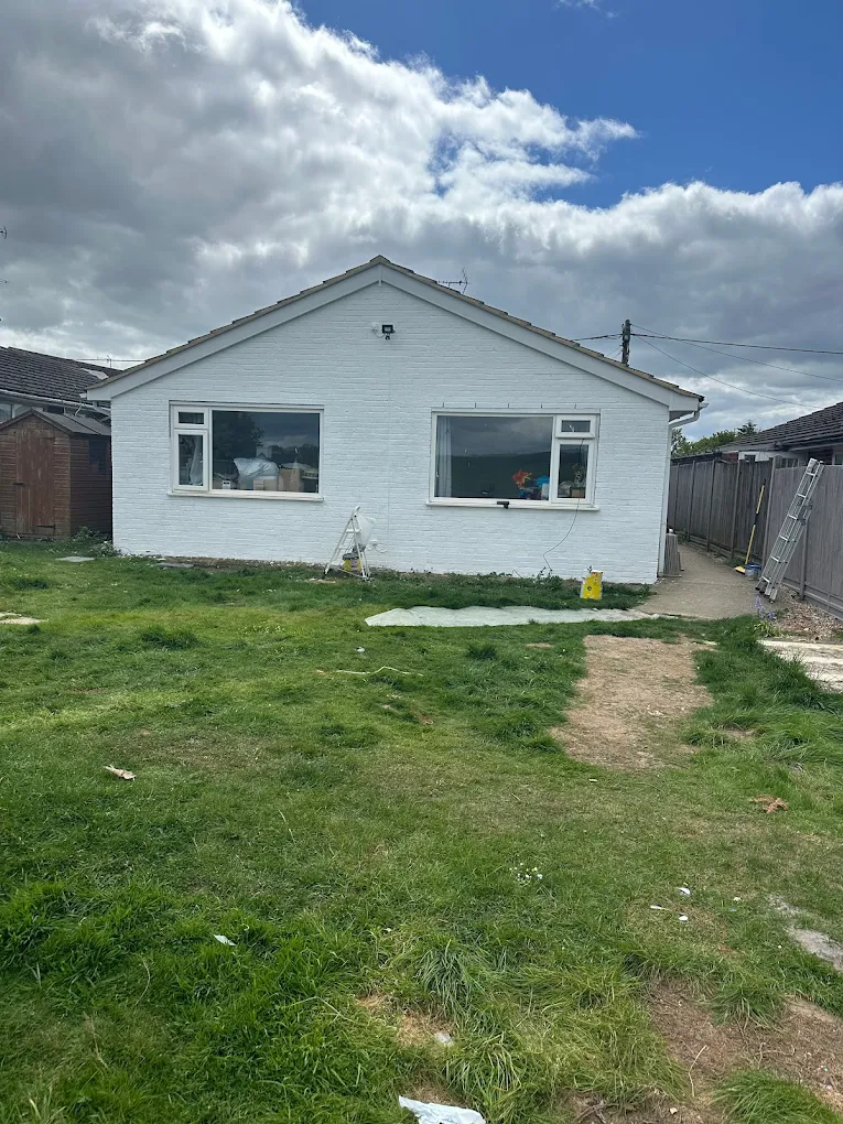 Back garden before landscaping — bare ground and rubble against a white bungalow